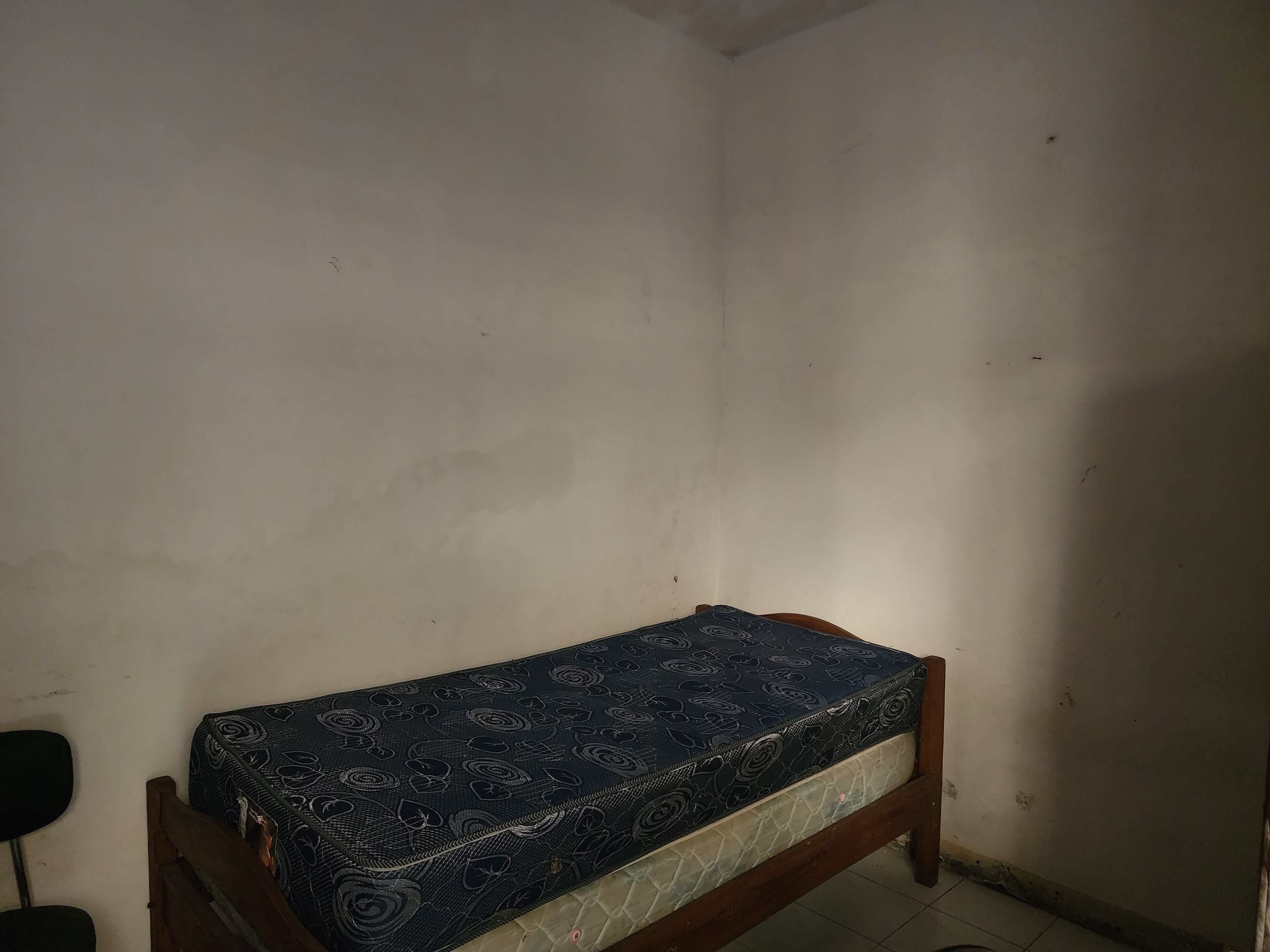 A small, dimly lit room with a single bed featuring a patterned mattress.