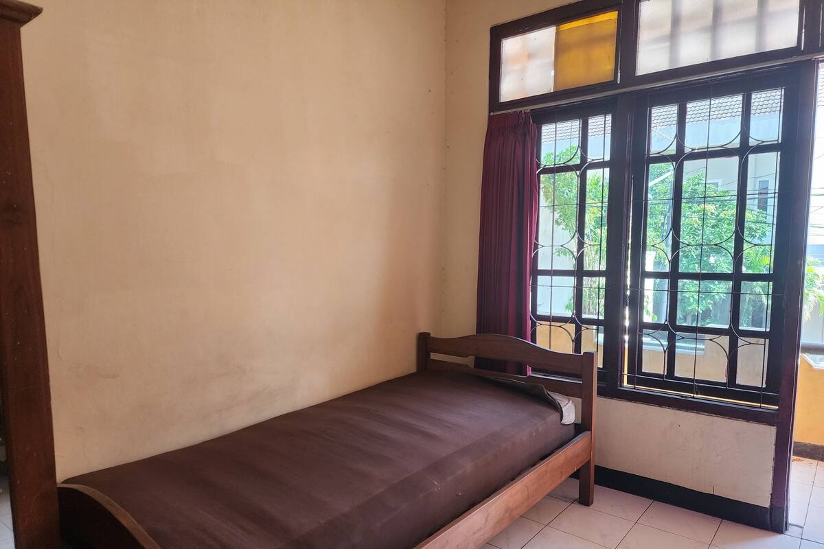 Ein Einzelbett in einem Zimmer mit Fenster und Blick auf Grün.