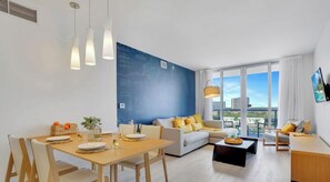A modern living room with a dining area, a sofa set, and a large window with a city view. - Spectacular View - Apt w/Balcony (Hallandale Beach)