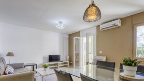 A modern living room with a glass dining table, a sofa, a TV, and a ceiling light fixture.