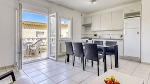 A modern kitchen with white cabinets, a dining area with a table and chairs, and a balcony with a view of a building with a tiled roof.