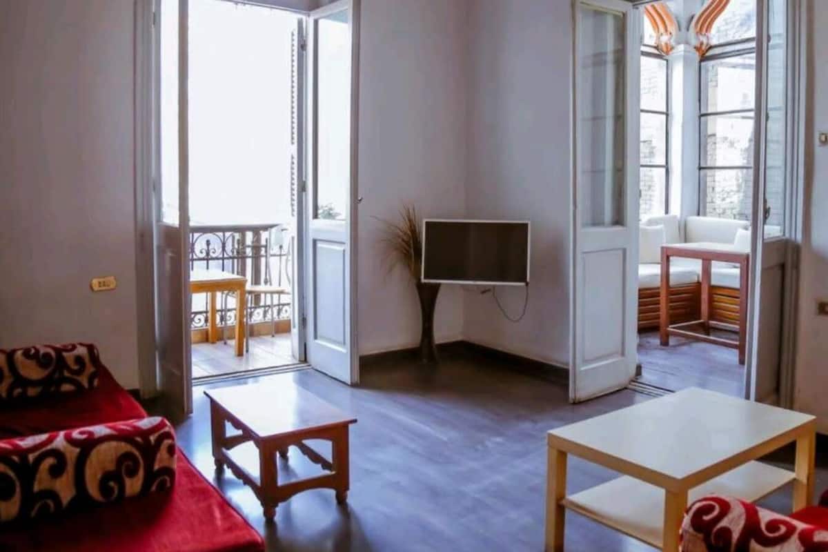 Habitación con televisión, sofá, una mesa y dos puertas abiertas que dan a balcones.