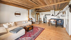 Ein gemütliches Wohnzimmer mit Holzboden, einer Couch, einem Couchtisch, einem gemusterten Teppich und einer Treppe, die in einen anderen Raum führt.