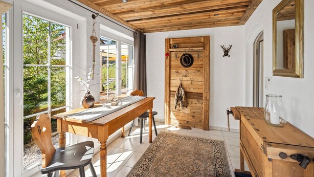 Ein Zimmer mit Holzboden, einem großen Fenster, einer Holztür mit Kleiderhaken und einem Spiegel an der Wand.