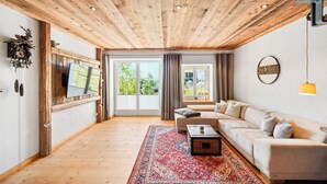 Ein geräumiges Wohnzimmer mit Holzboden, einem großen Sofa, einem Couchtisch und einem gemusterten Teppich.