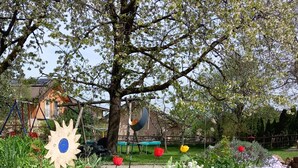 A garden with a variety of flowers, a swing set, and a tree. - Ferienwohnung Gaisberg (Ainring)