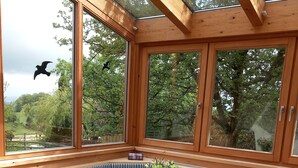 A cozy dining area with a wooden table, blue-striped bench seating, and large windows offering a view of trees and a bird flying outside. - Ferienwohnung Gaisberg (Ainring)