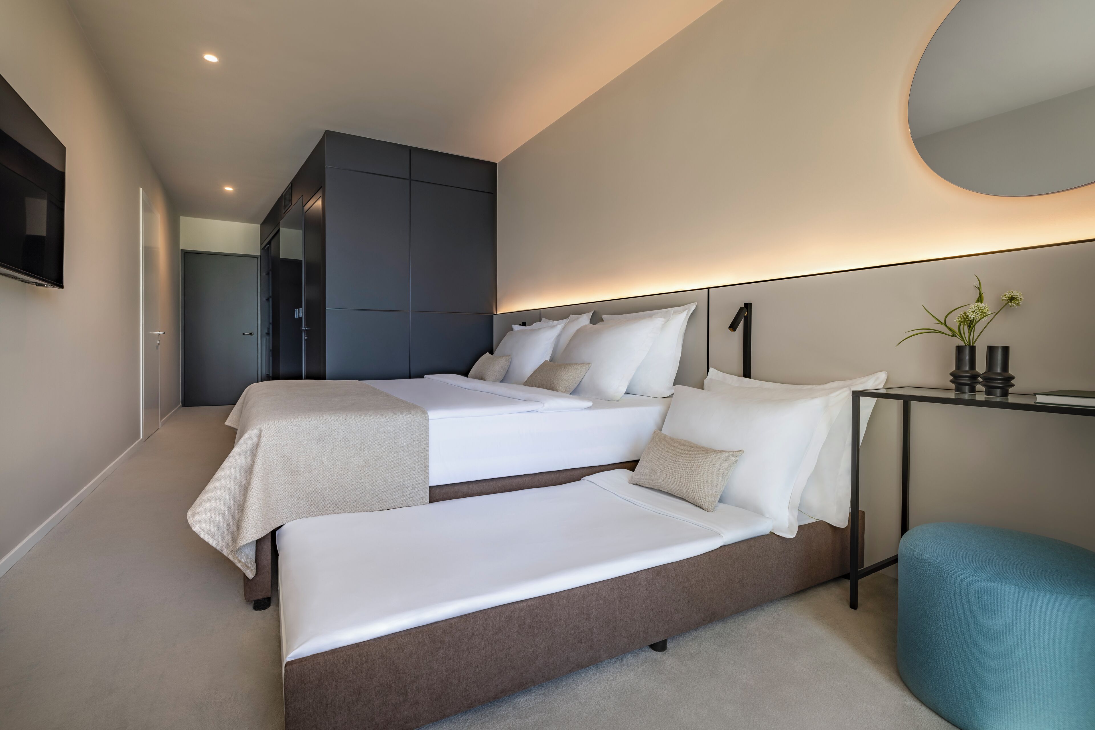 A modern bedroom with two beds, a large mirror, and a small table with a plant.