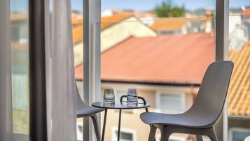 A balcony with a table and two chairs, overlooking a residential area with red-tiled roofs.