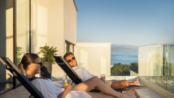 A couple relaxing on a balcony with a glass barrier, overlooking a scenic view.