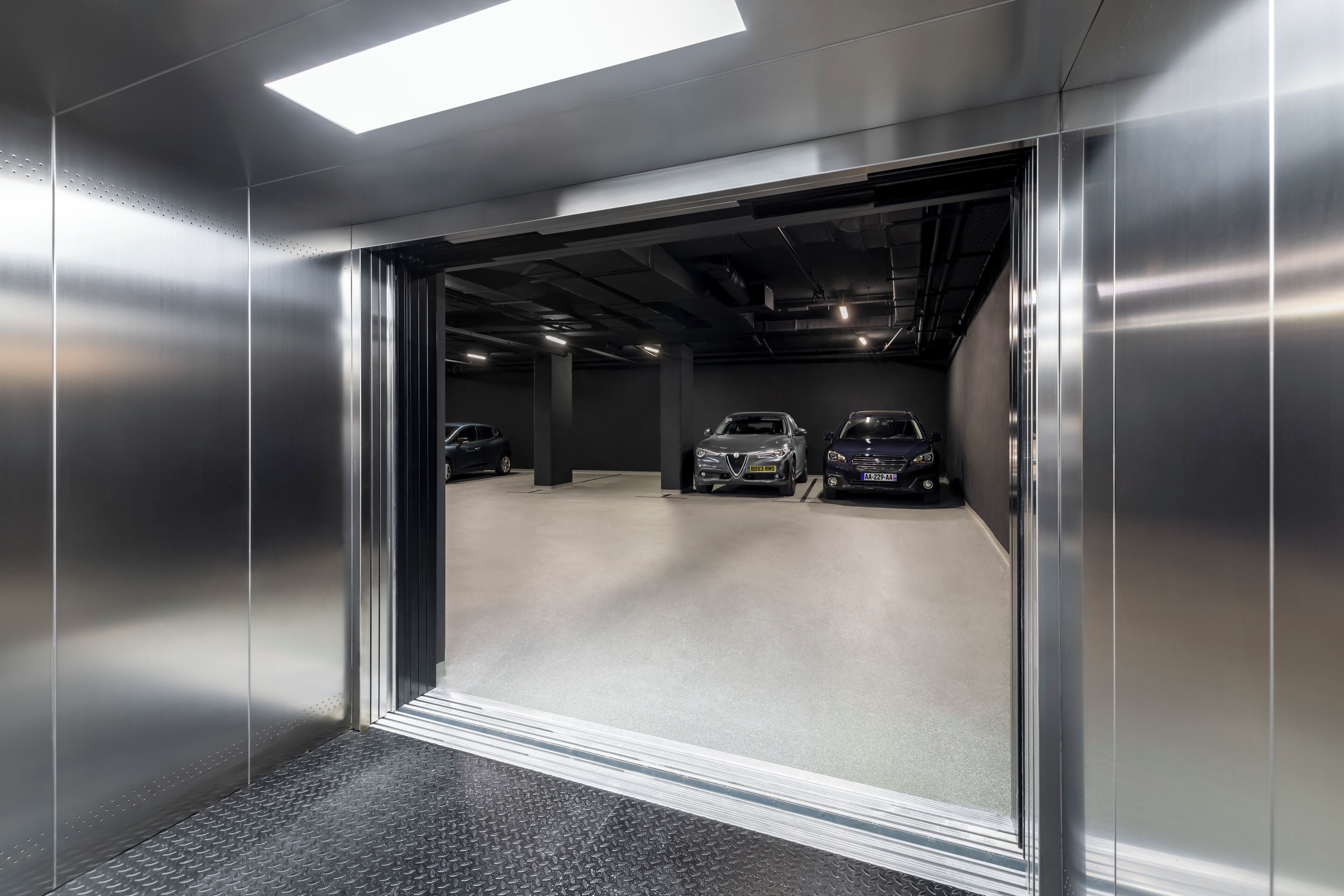 Un ascensor con interior metálico y vistas a un aparcamiento con varios coches.