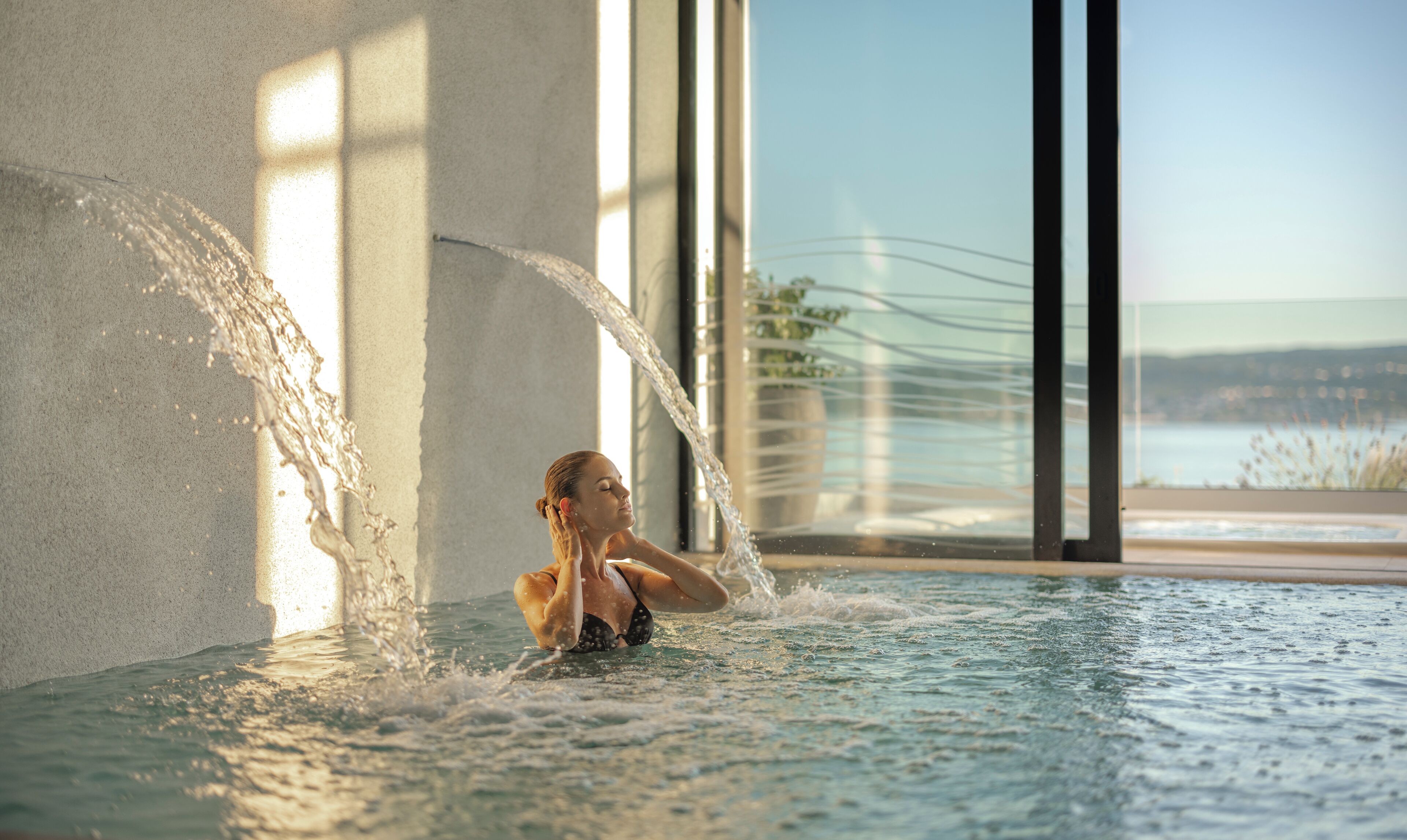 A person in a water feature with a view of a body of water and a building in the background.