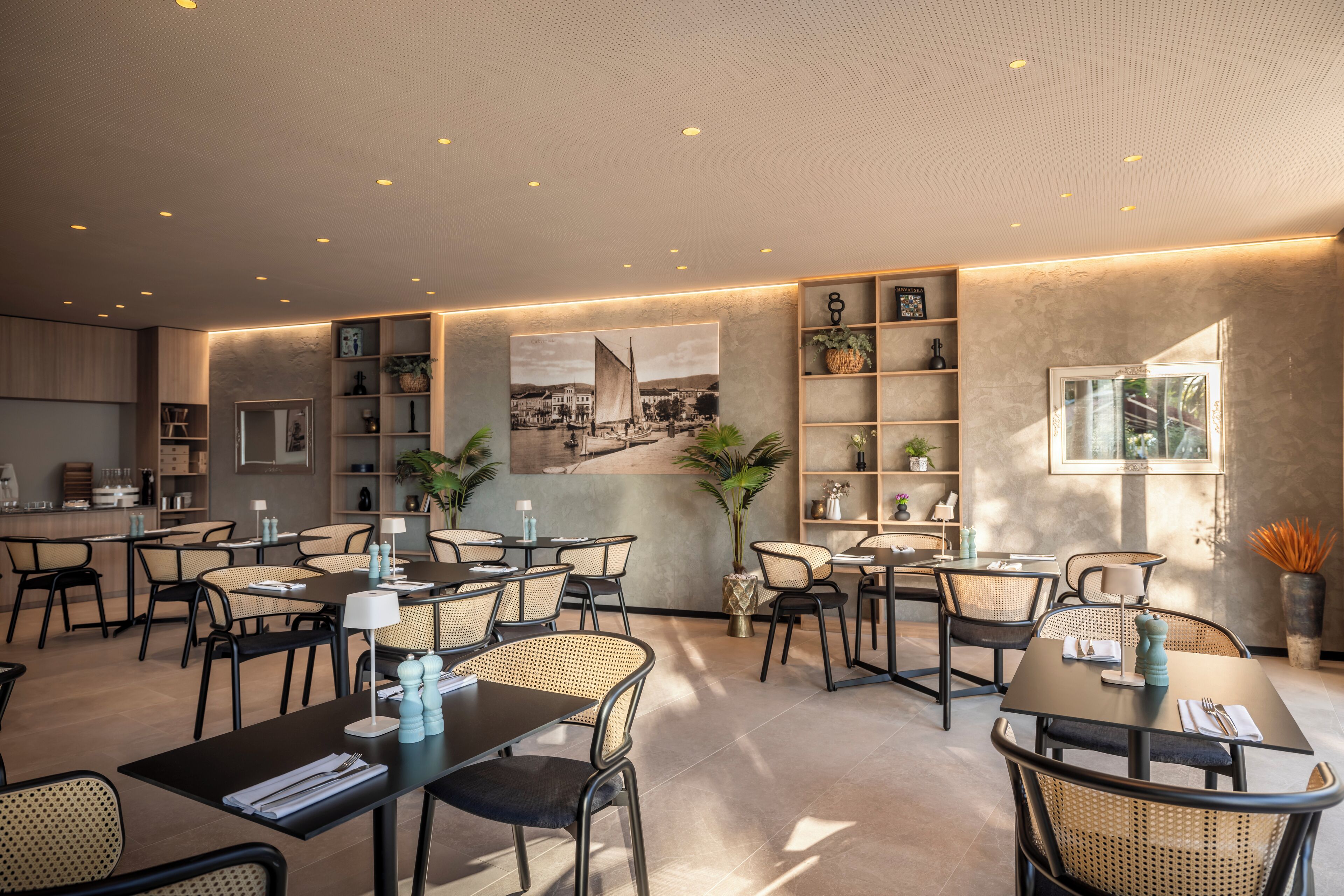 Un espace de restauration moderne, doté de plusieurs tables et chaises, d’un grand tableau au mur et d’étagères ornées d’objets décoratifs.