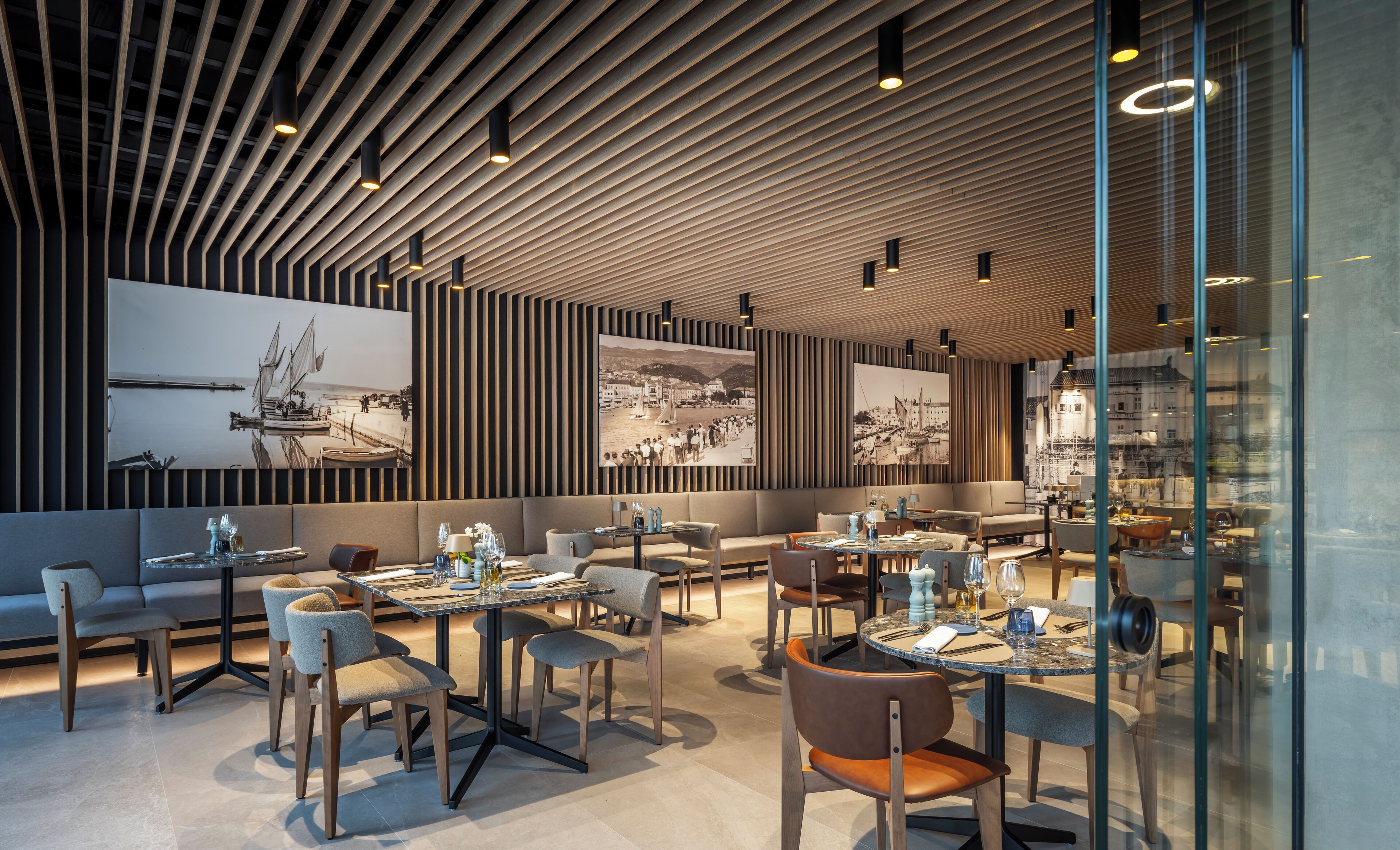 Een modern restaurant met een houten plafond, grote schilderijen en een combinatie van zitplaatsen, waaronder tafels en banken.