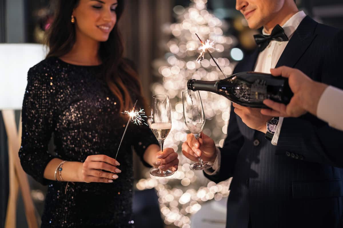 A person holding a champagne bottle, pouring into two glasses with sparklers.