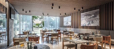Een modern restaurant met ronde tafels, stoelen en een grote foto aan de muur.