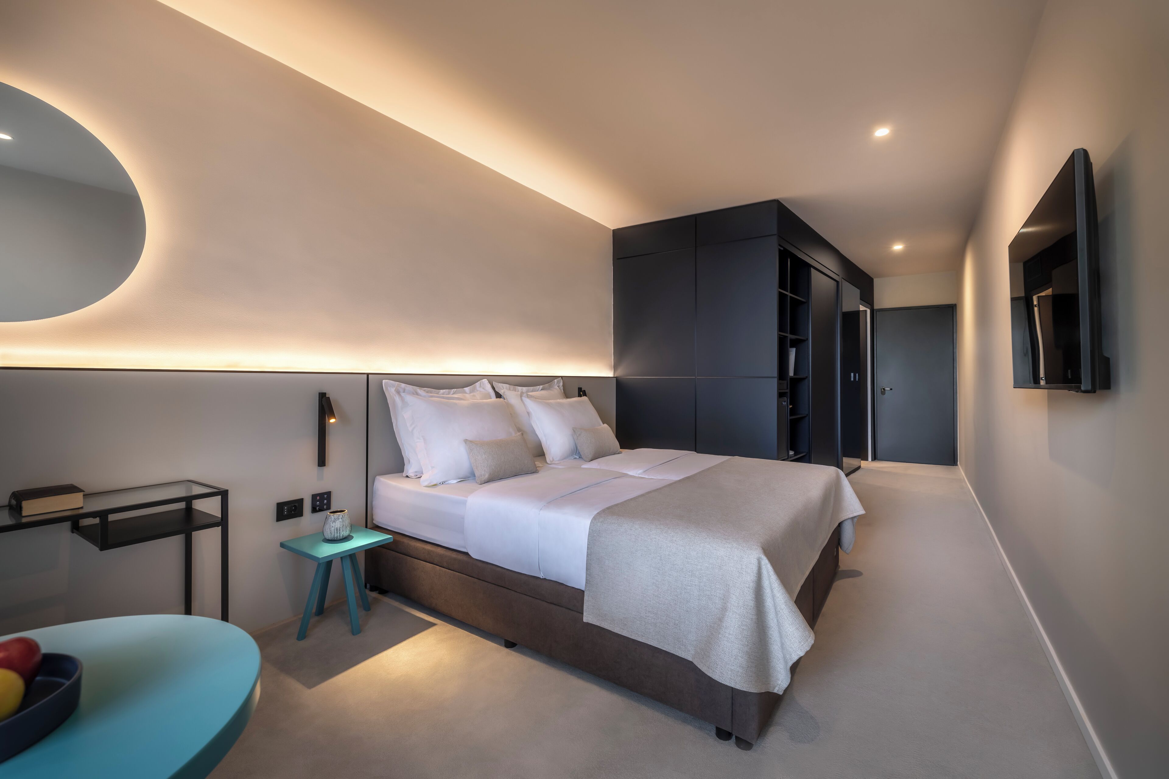 A modern bedroom with a large bed, bedside tables, a wardrobe, and a mirror.