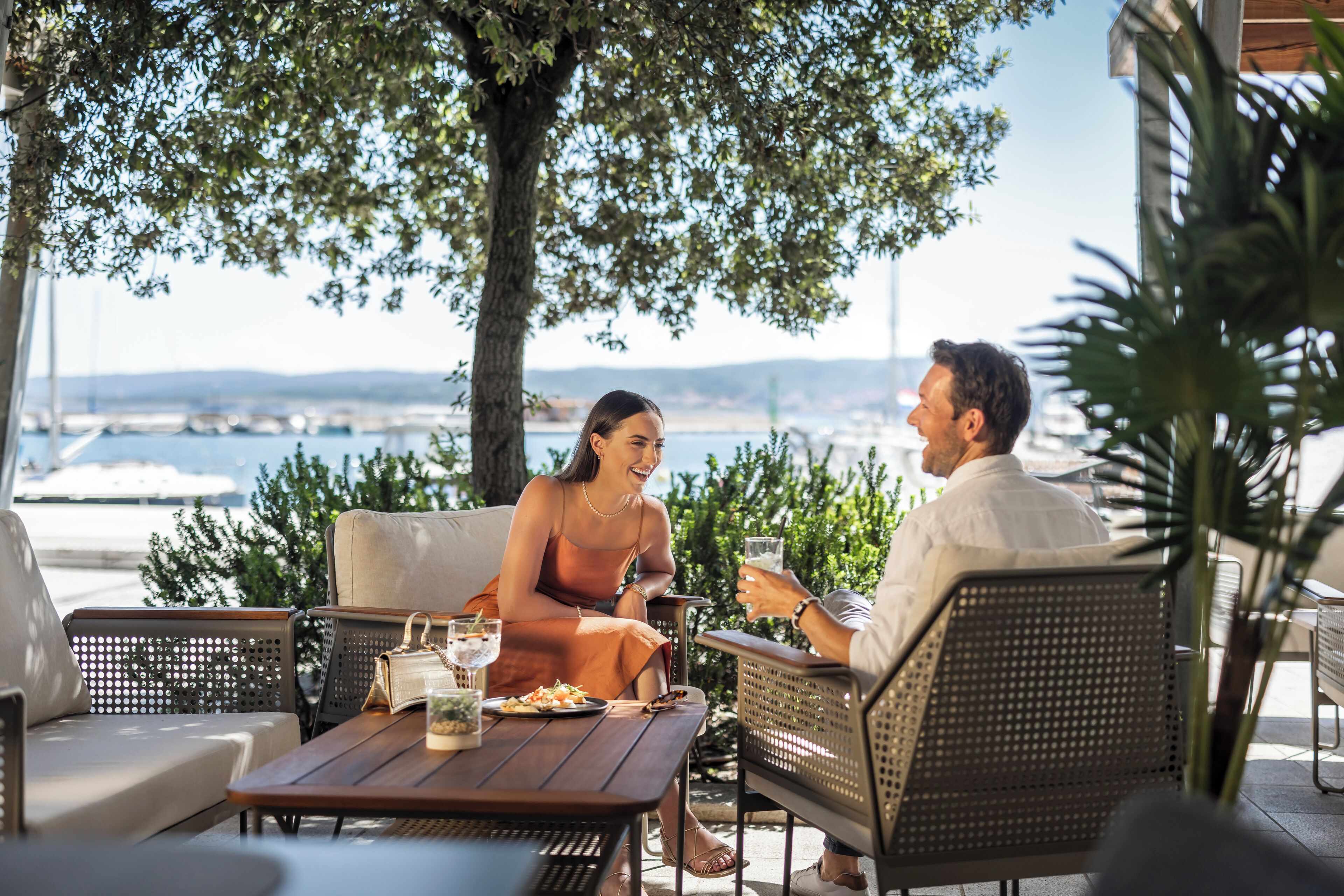 An outdoor seating area with wicker furniture, a wooden table, and a view of the sea.