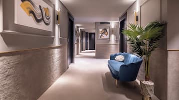 Un couloir moderne avec un fauteuil bleu, une plante en pot et des œuvres d’art abstraites accrochées au mur.