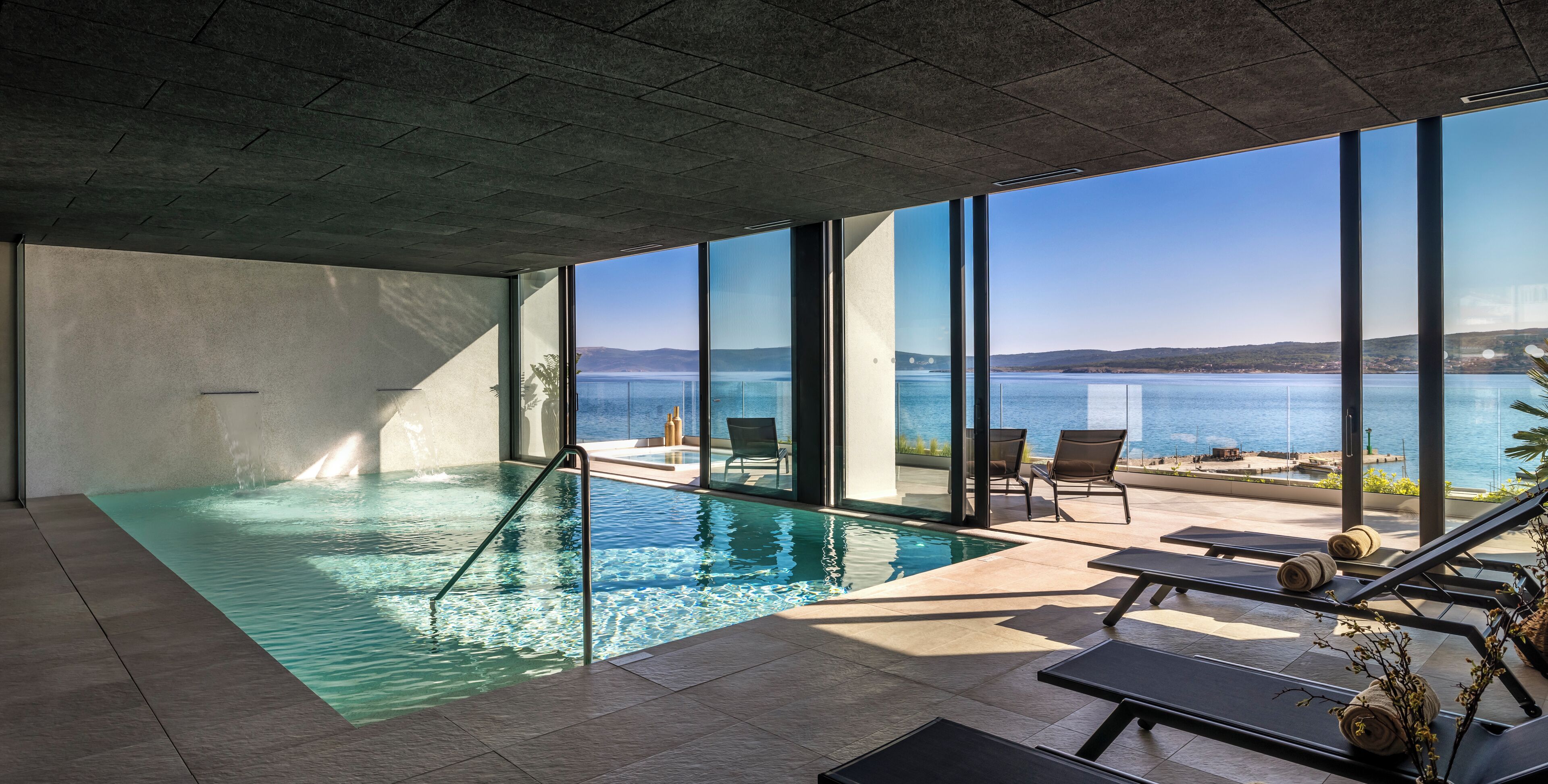 A modern indoor swimming pool with clear views of the sea and hills.