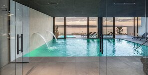 A modern indoor pool with clear glass walls, a view of the sea, and lounge chairs. - Aminess Younique Narrivi Hotel (Crikvenica)