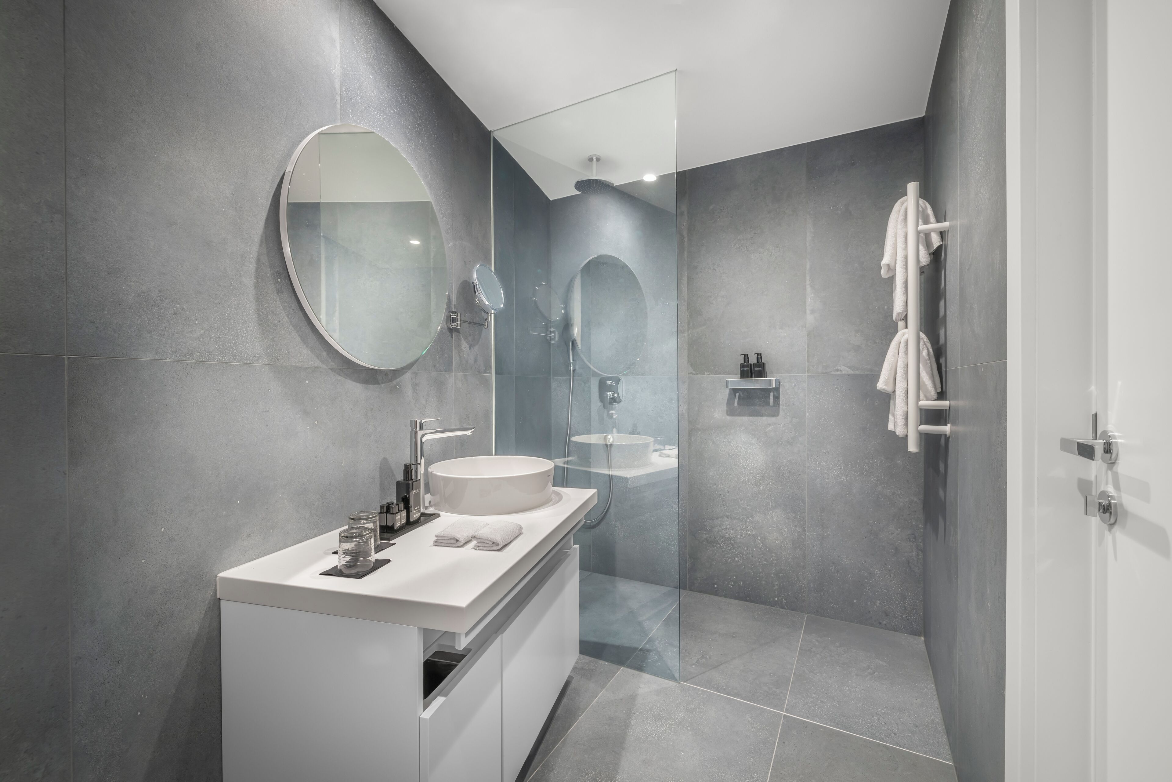 Un baño moderno con un espejo grande, un lavamanos redondo y una zona de ducha con cerramiento de vidrio.
