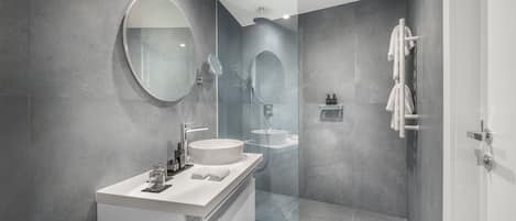 Un baño moderno con un espejo grande, un lavamanos redondo y una zona de ducha con cerramiento de vidrio.