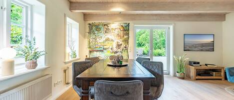 A dining area with a wooden table, cushioned chairs, and a large window with a view of greenery.