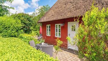 A red house with a thatched roof, a patio with outdoor furniture, and lush greenery surrounding the property.