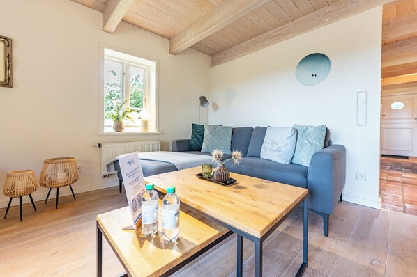 Un salon moderne avec une table basse en bois, un canapé avec des coussins, des fauteuils en osier, une fenêtre donnant sur un beau paysage et une horloge murale.