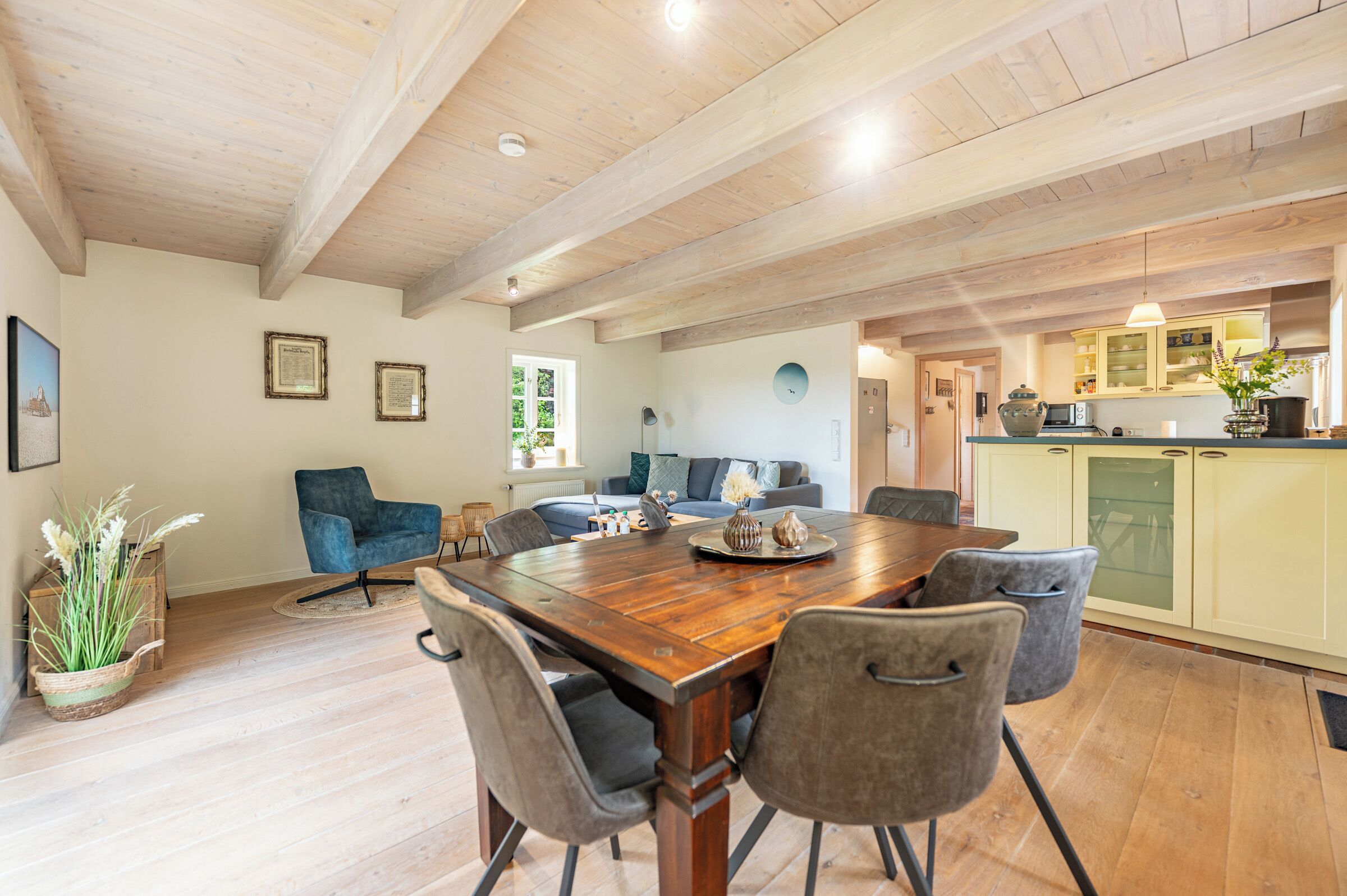 A spacious dining area with a wooden table, grey upholstered chairs, and a view into the kitchen.