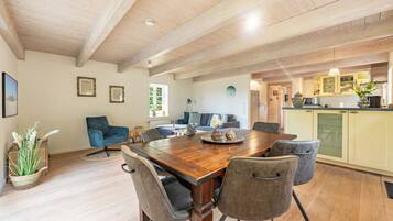 A spacious dining area with a wooden table, grey upholstered chairs, and a view into the kitchen.