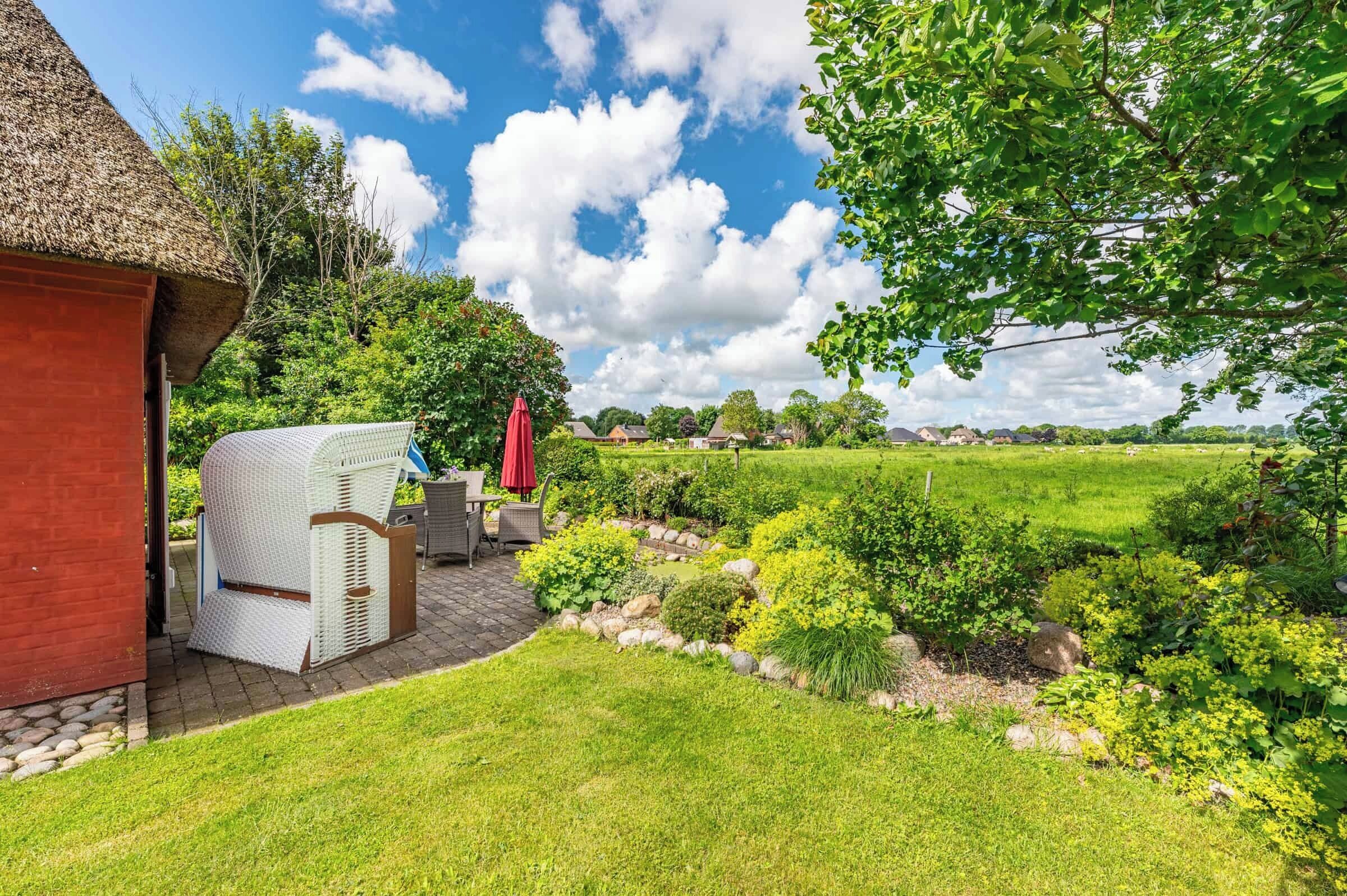 Een tuin met een rieten constructie, een overdekte zithoek en uitzicht op een groen veld.