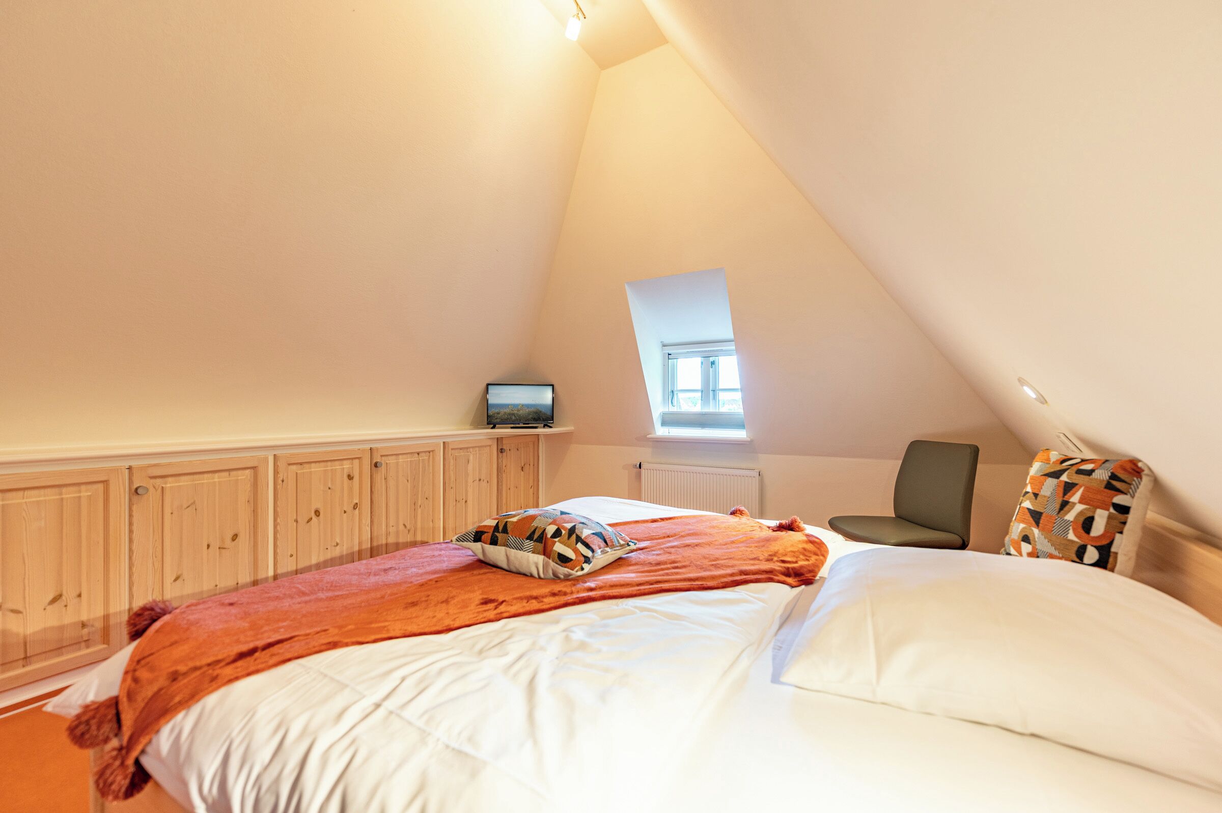 A bedroom with a bed, a television, a chair, and a window.