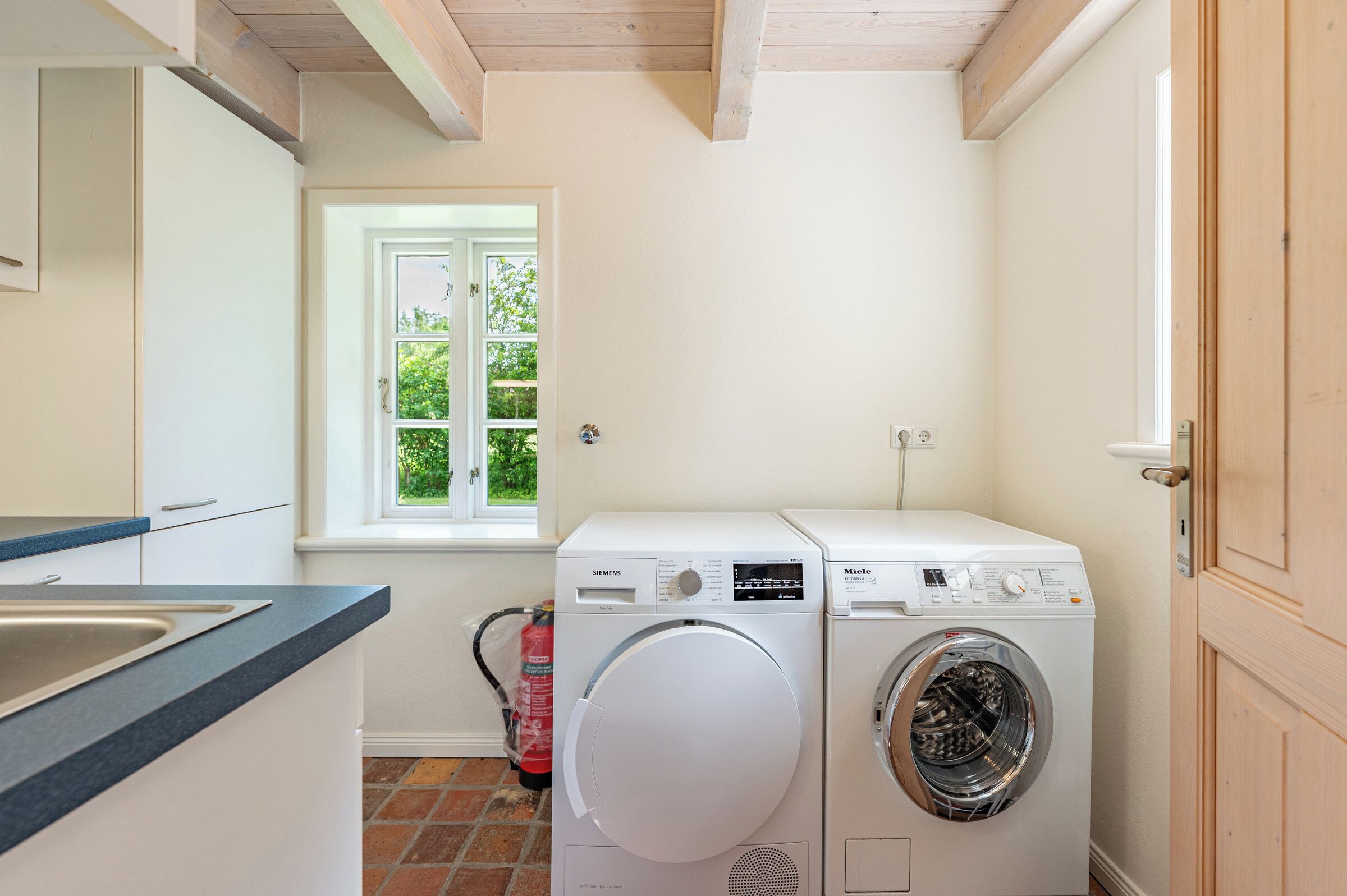 A laundry room with a Siemens and Miele washing machine, a window, and a fire extinguisher.