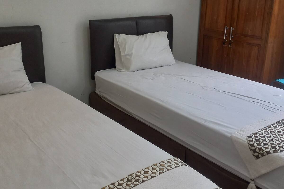 Two single beds with dark headboards and white bedding, a wooden wardrobe, and a patterned bed runner.