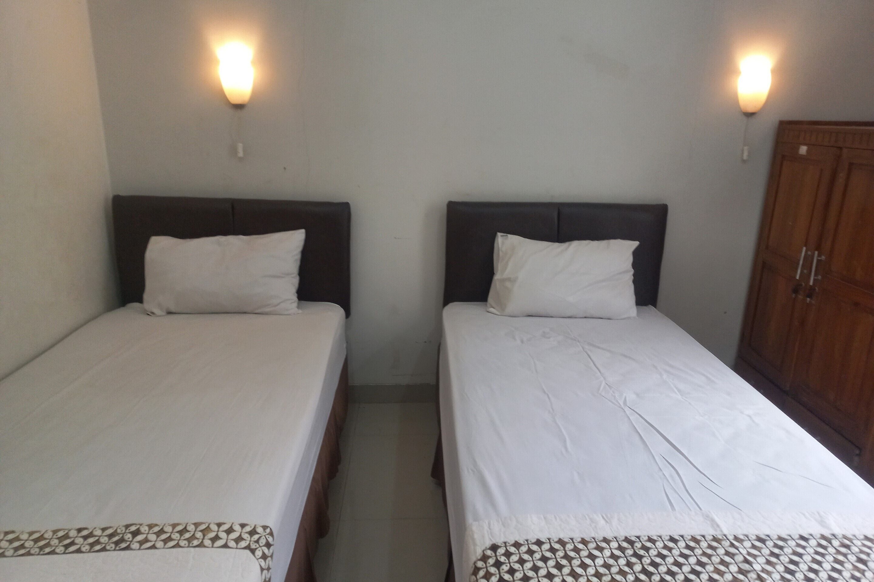 Two single beds with headboards, white bedding, and wall-mounted lights.