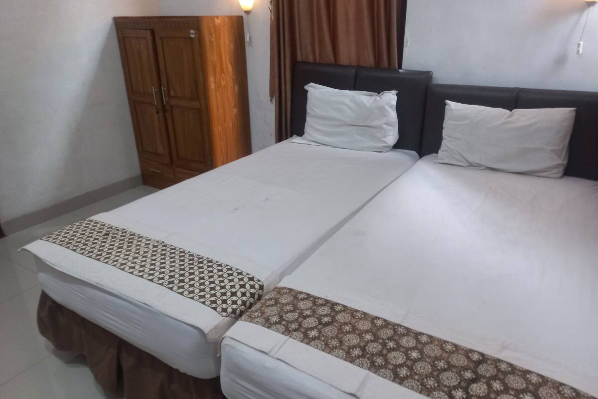 A double bed with white and patterned bedspreads, a wooden wardrobe, and a wall-mounted light fixture.
