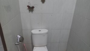 A small, tiled bathroom with a toilet, a showerhead, and a toilet brush.