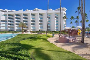 A hotel with a pool, palm trees, and a children's play area.