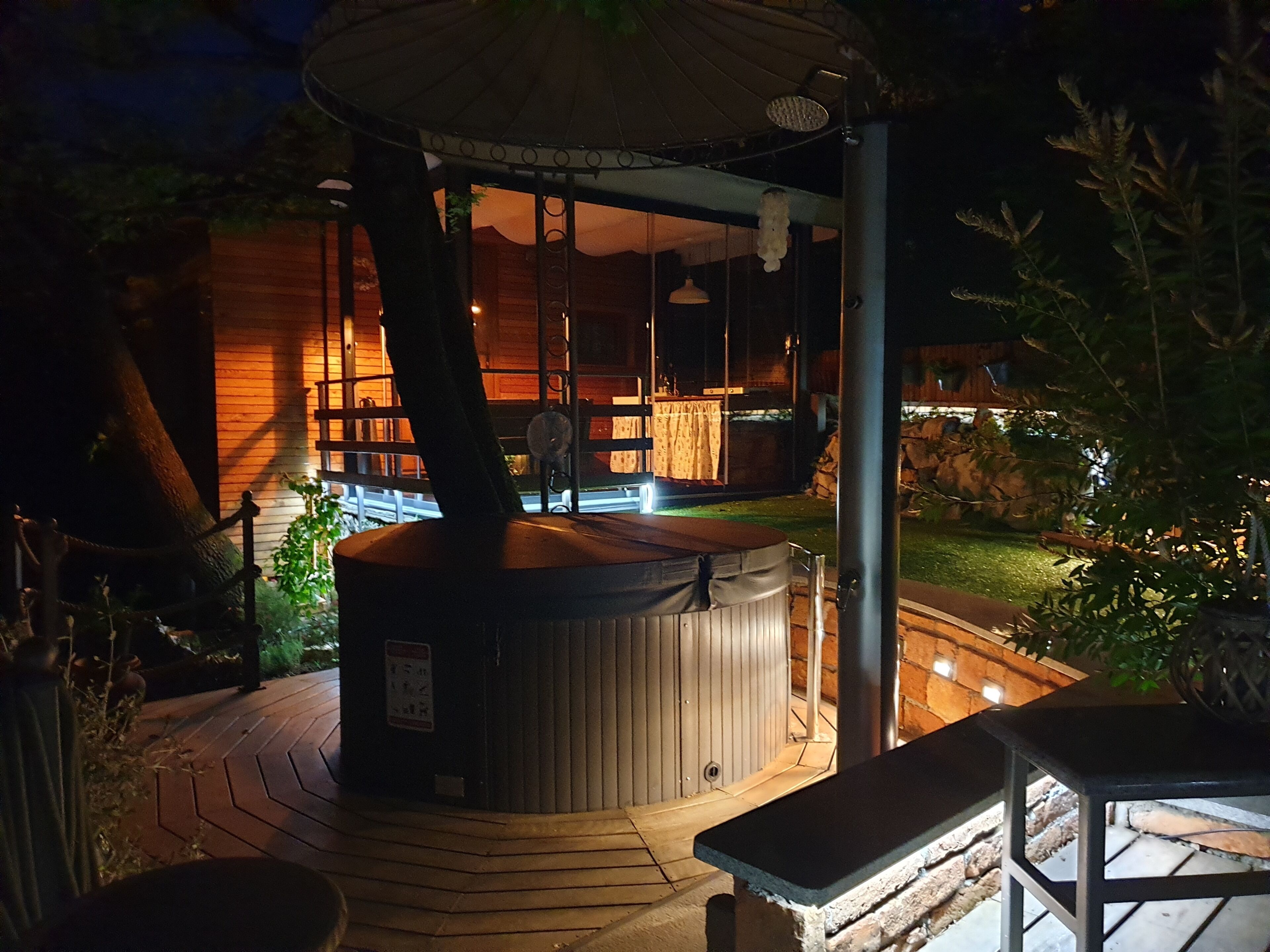 Een hoek met een bubbelbad, een houten terras, een pergola en uitzicht op een gebouw met grote ramen.