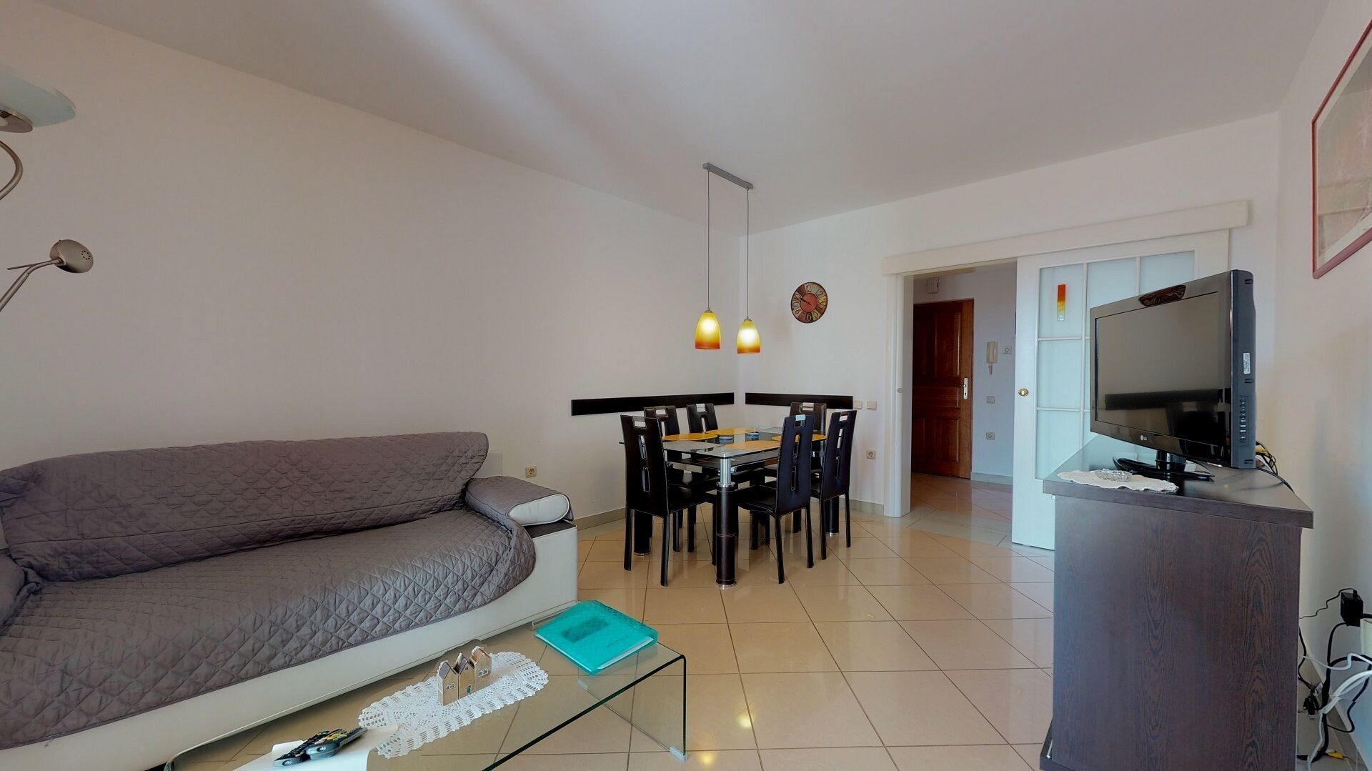 Uma sala de estar com sofá, mesa de centro, televisão e um espaço de jantar com cadeiras e mesa.