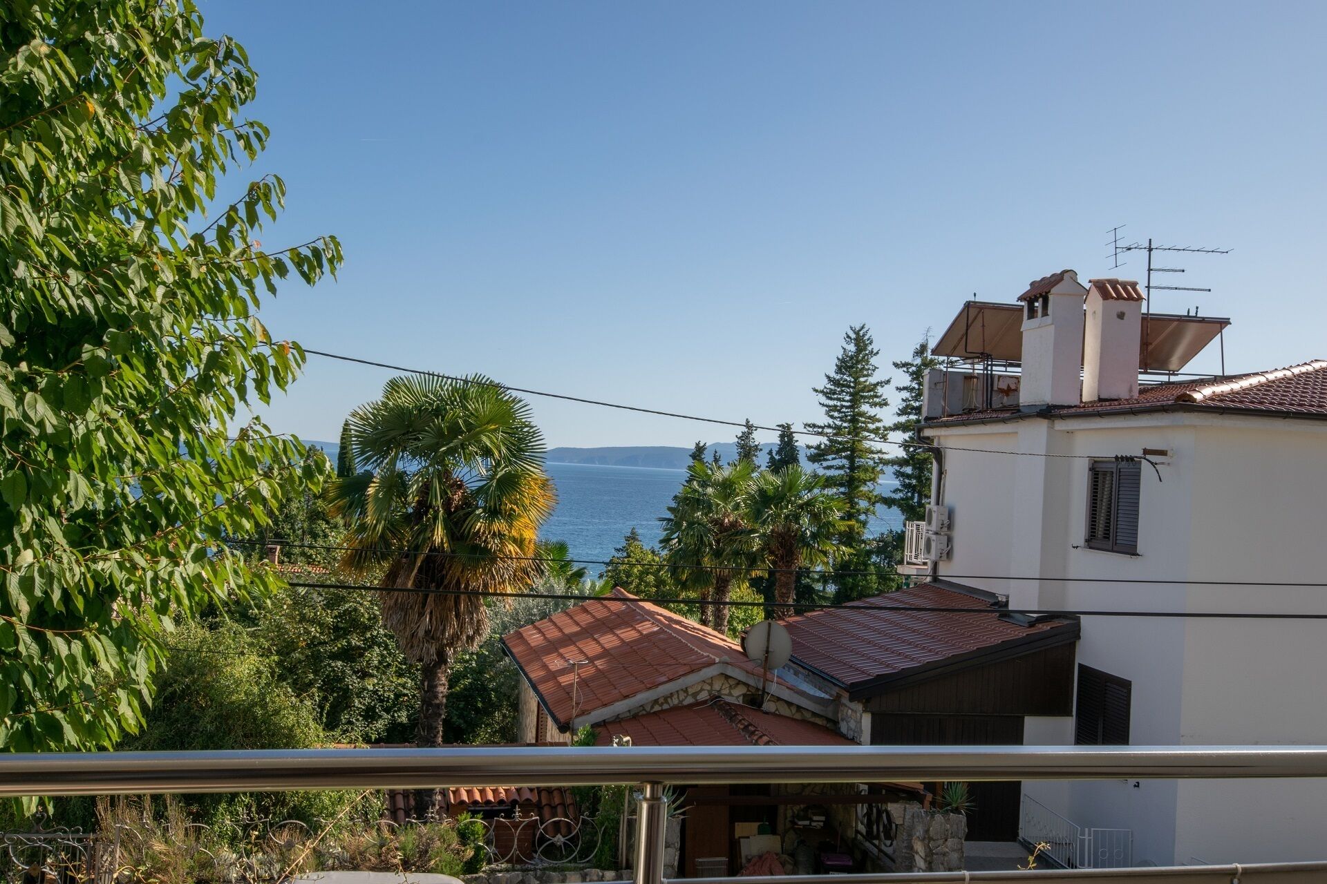 A residential area with a view of the sea, featuring houses with red-tiled roofs and a white building with a satellite dish.