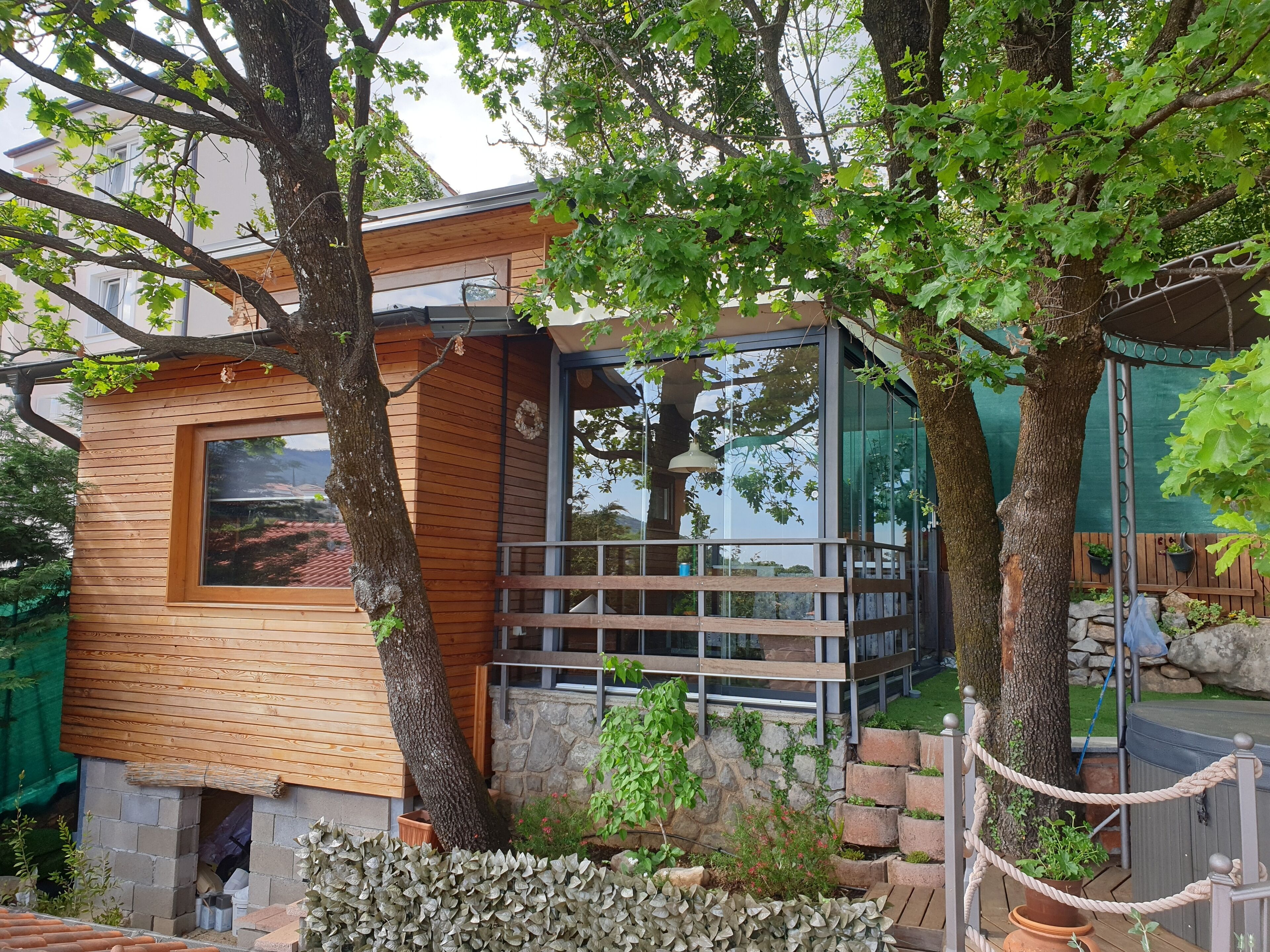 Una cabana de fusta moderna amb una ampliació de vidre, envoltada d'arbres i una paret de pedra.