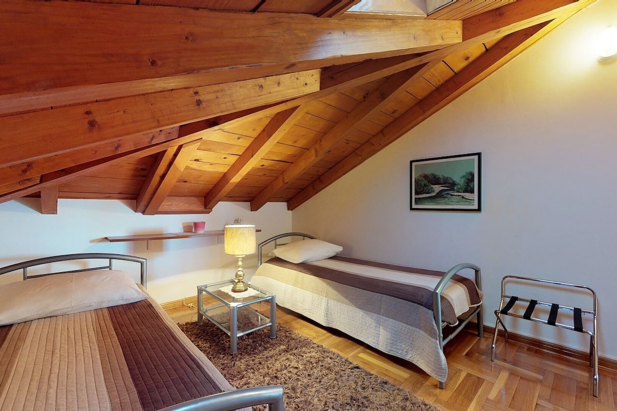 Une chambre mansardée chaleureuse avec deux lits, une petite table avec une lampe et une chaise en métal.