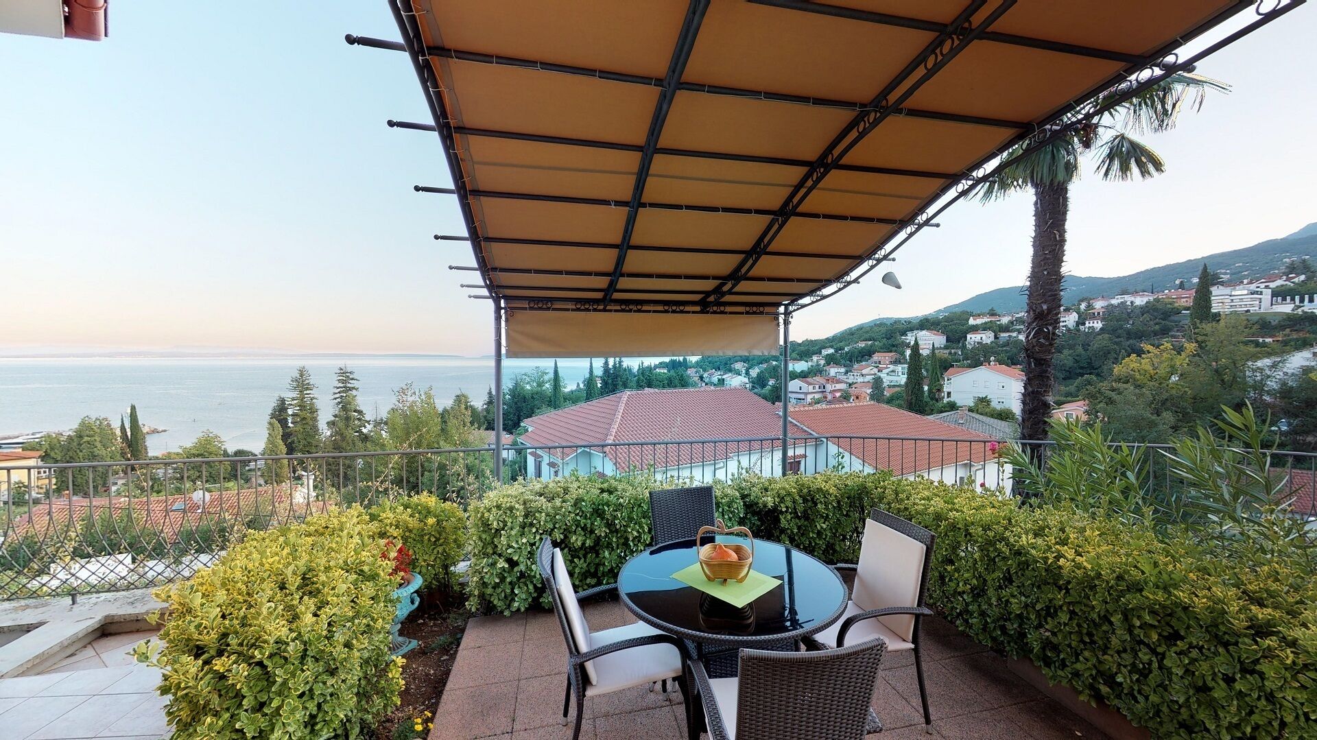 Eine Terrasse mit Tisch und Stühlen, Blick auf das Meer und eine Stadt im Hintergrund.