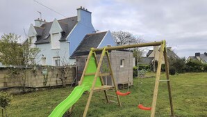 A wooden swing set with a green slide in a grassy yard. - Petite Maison Proche Mer, Jardin Clos, Près du GR 34 et du Bourg , Chien Accepté (Plouguerneau)