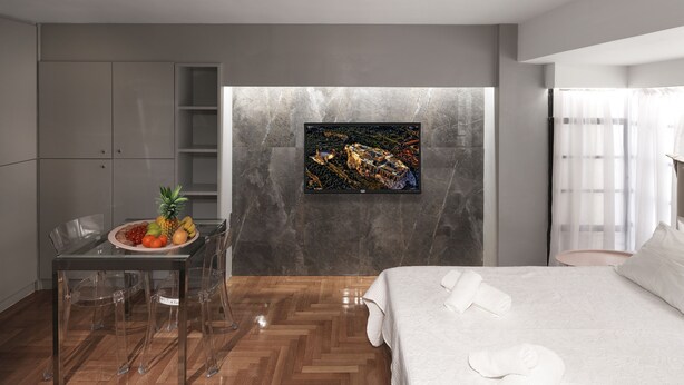 Una habitación de hotel moderna con cama, una mesa de comedor con fruta, una silla transparente, un armario y una obra de arte colgada en la pared.