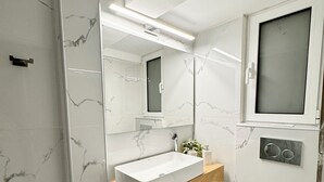 Un baño moderno con un lavamanos rectangular, un espejo, un inodoro y un cubo de basura pequeño.
