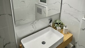 Un baño moderno con un lavabo blanco, un espejo y paredes de mármol.